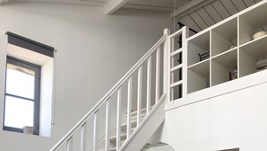 Eine Treppe mit weißen Geländern führt zu einer zweiten Etage. Eine kleine Vitrine mit Dekoration steht daneben.