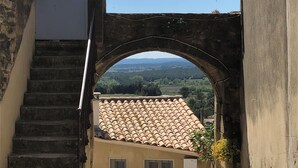 Eine Steintreppe führt zu einem rundbogigen Eingang, mit Blick auf ein Gebäude mit Ziegeldach in der Ferne.
