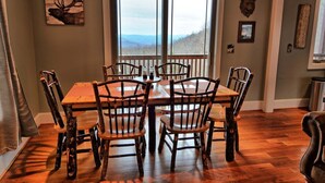 A dining area with a wooden table and chairs, a large window with a view, and rustic decor. - Experience serenity in this 3-bedroom cabin with stunning views in West Jefferson, NC. (West Jefferson)