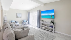 A modern living room with a large flat-screen TV, a sofa, a coffee table, and a TV stand with decorative items.