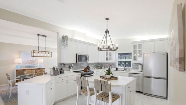 A modern kitchen with white cabinetry, a central island, bar stools, and a hanging light fixture.