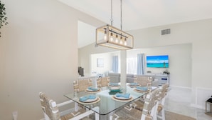 A dining area with a glass table, wicker chairs, and a hanging light fixture.