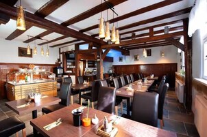 A restaurant with wooden beams, long tables, and hanging pendant lights.