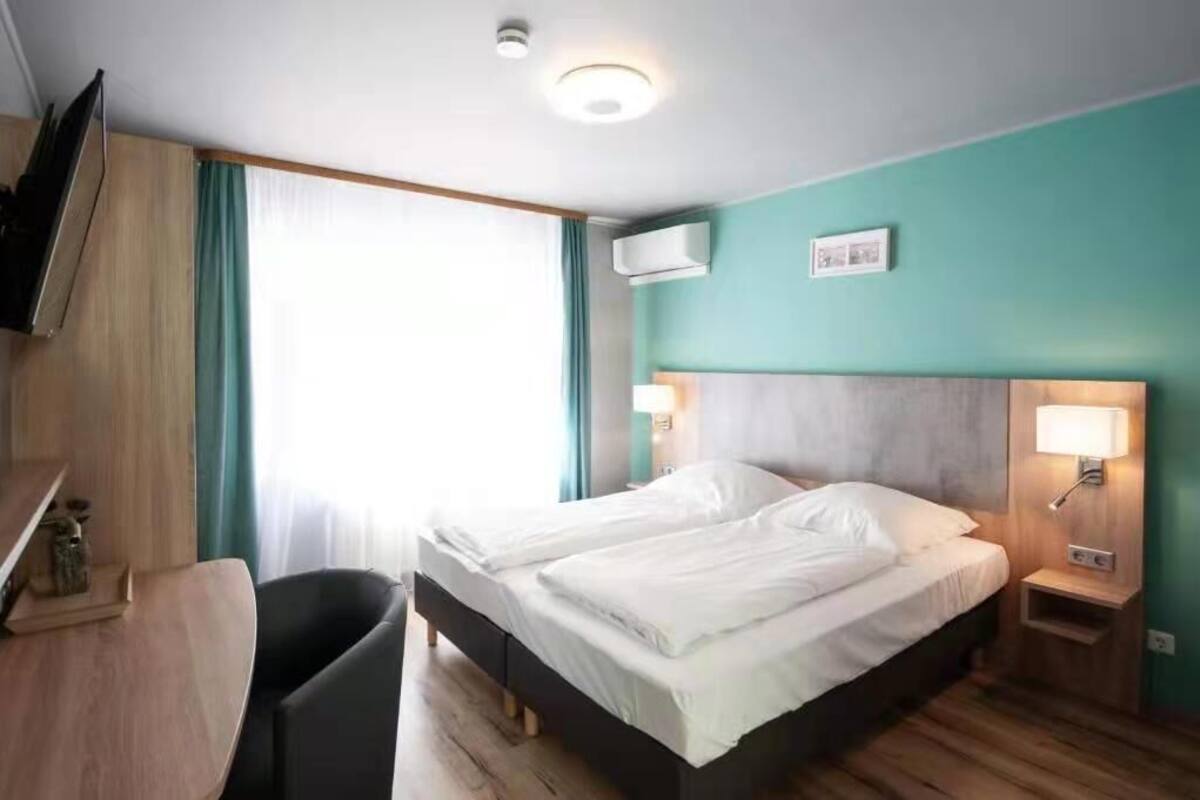 A hotel room with a bed, bedside tables, a desk, a chair, and a TV.