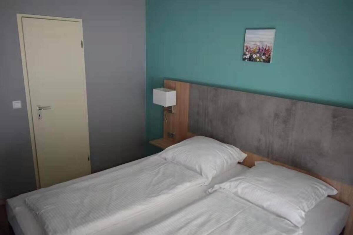 A single bed with white bedding in a room with teal walls, a wooden headboard, and a small bedside table with a lamp.
