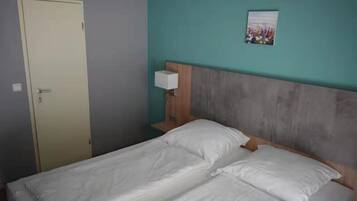 A single bed with white bedding in a room with teal walls, a wooden headboard, and a small bedside table with a lamp.