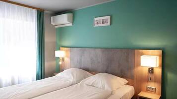 A hotel room with a bed, two bedside lamps, an air conditioning unit, and a framed picture on the wall.