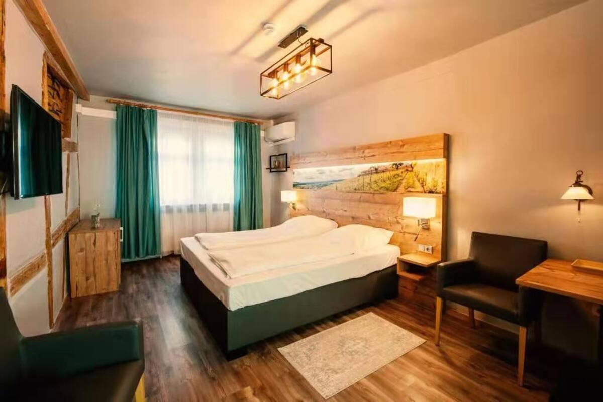 A hotel room with a bed, a desk, a chair, a TV, and a painting on the wall.
