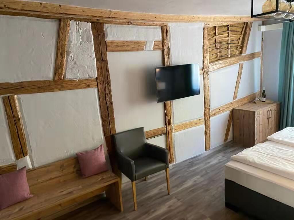 A room with a bed, a wooden bench with cushions, a TV mounted on the wall, and a wooden cabinet.