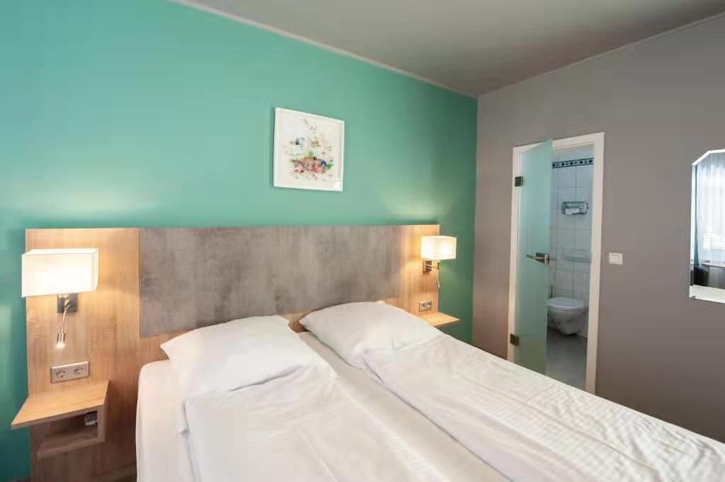 Ein Hotelzimmer mit einem Bett, zwei Nachttischlampen, einem Nachttisch, einem Spiegel und einer Tür zu einem Badezimmer.
