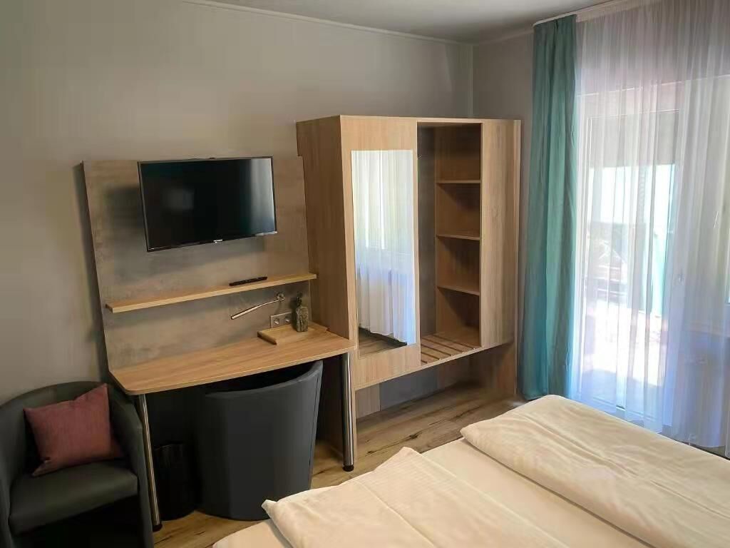 A hotel room with a bed, a desk with a TV, a wardrobe, and a window with curtains.