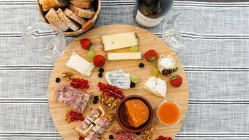 Un tagliere con diversi formaggi, frutta, noci e salumi, accompagnato da bicchieri da vino e una bottiglia.