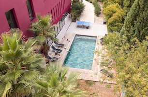 Una piscina en la azotea con terraza de madera, sillones de descanso y mesa de tenis.