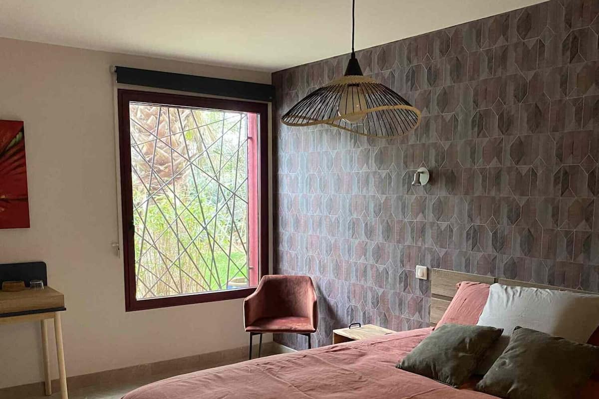 Un dormitorio con una cama grande, una silla, un escritorio y una ventana con vistas a zonas verdes.