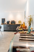 Una cocina moderna con comedor, que incluye un mostrador con alimentos, una máquina de café y un florero con flores.