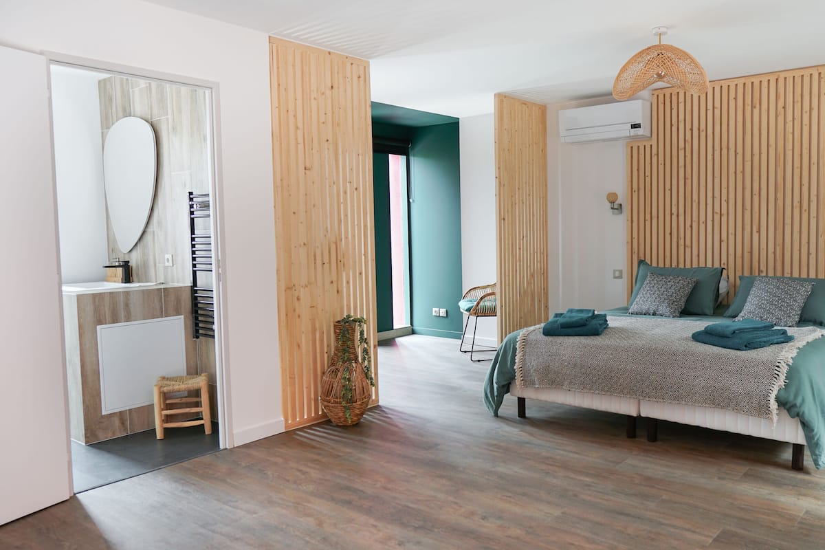 Un dormitorio moderno con una cama, cabecera de madera, mesita de noche, espejo y una silla de mimbre.