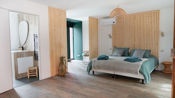 Un dormitorio moderno con una cama, cabecera de madera, mesita de noche, espejo y una silla de mimbre.