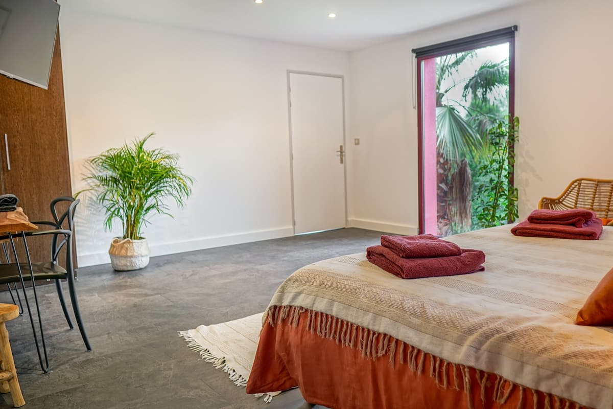 Un dormitorio con cama, una silla, una mesa y una planta en maceta.