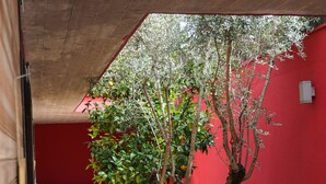 A covered outdoor area with a red wall, a tree, and a tiled floor. - Villa Magnolia (Montpellier)