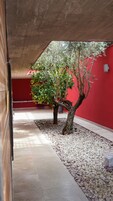 Un espacio al aire libre techado con una pared roja, un árbol y suelo de baldosas.