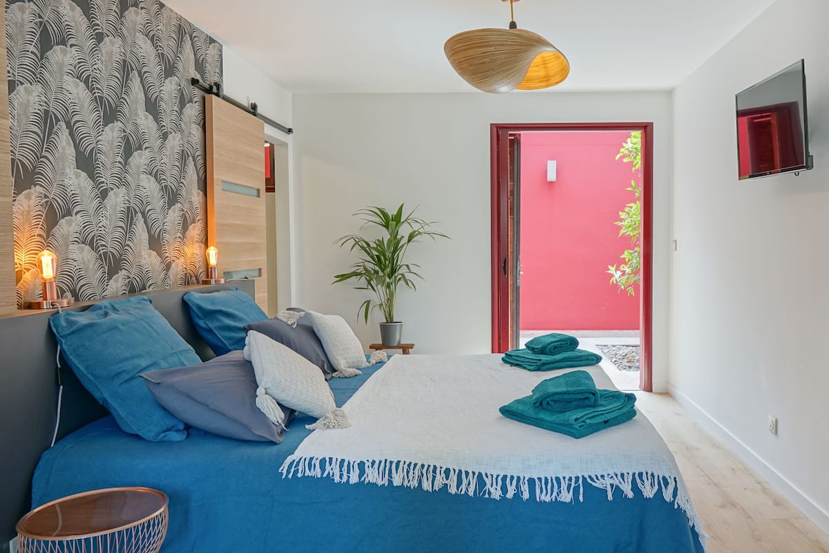 Un dormitorio con cama, lámpara de noche, planta en maceta y vistas al exterior.