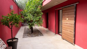 A narrow corridor with a red wall, a potted tree, and a closed wooden door. - Villa Magnolia (Montpellier)