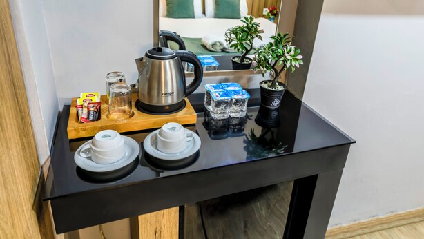 Habitació d'hotel amb una taula negra que presenta una tetera, sobres de te, gots i una planta en test.