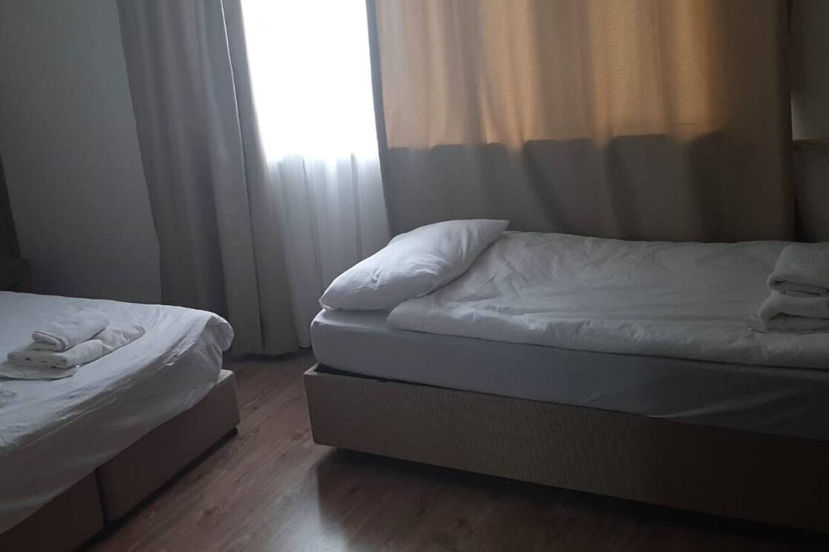 A hotel room with two beds, wooden headboard, and a window with curtains.