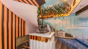 Habitació amb un mural que representa un pont i un paisatge urbà, una taula de recepció i una paret amb franges.