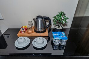 A kitchen counter with a kettle, teapots, glasses, a potted plant, and bottled water.