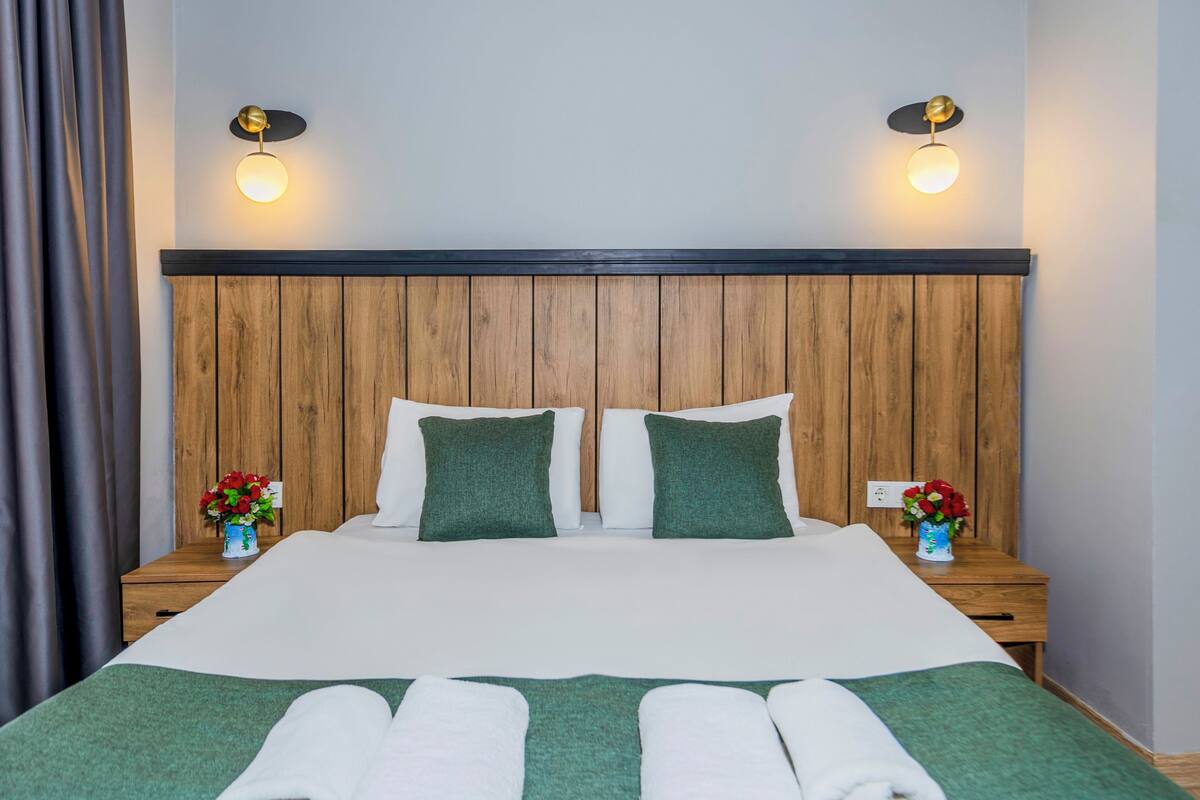 A neatly made bed with two pillows, a wooden headboard, and two bedside tables with lamps.