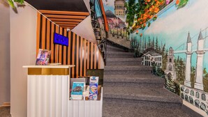 Una escala amb un mural d'un paisatge urbà, una taula de recepció amb una televisió de pantalla plana i fulletons.
