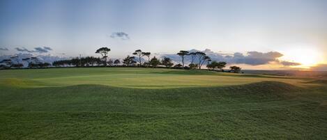 Un campo de golf con cielo despejado y una puesta de sol al fondo.