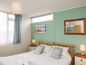 A bedroom with a bed, bedside tables, a nightstand, a window with curtains, a painting, and a mirror. - Fairway Lodge (Kingsbridge)