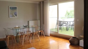 Ein Essbereich mit einem Glastisch und Stühlen, einem großen Fenster mit Blick auf Gartenmöbel und einem Wandbild.