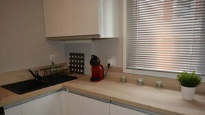 Eine Küche mit einem schwarzen Spülbecken, einem roten Wasserkocher, einer Topfpflanze und einem Fenster mit Jalousien.