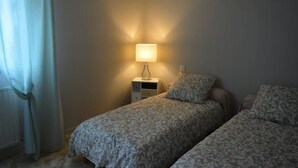 Ein Schlafzimmer mit zwei Betten, einem Nachttisch mit Lampe und einem Fenster mit Vorhängen.