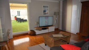 Ein Wohnzimmer mit Fernseher, einer Couch, einem Couchtisch und Gartenblick durch eine Schiebetür.