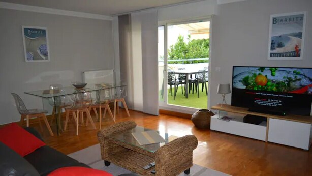 Ein Wohnzimmer mit Glastisch, Rattan-Sofa und Flachbildfernseher.