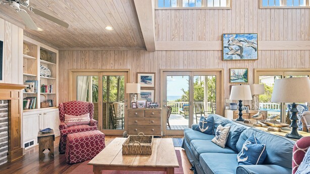 Ein geräumiges Wohnzimmer mit Holzbalkendecke, einem blauen Sofa, einem rot gemusterten Sessel und einem Couchtisch aus Holz.