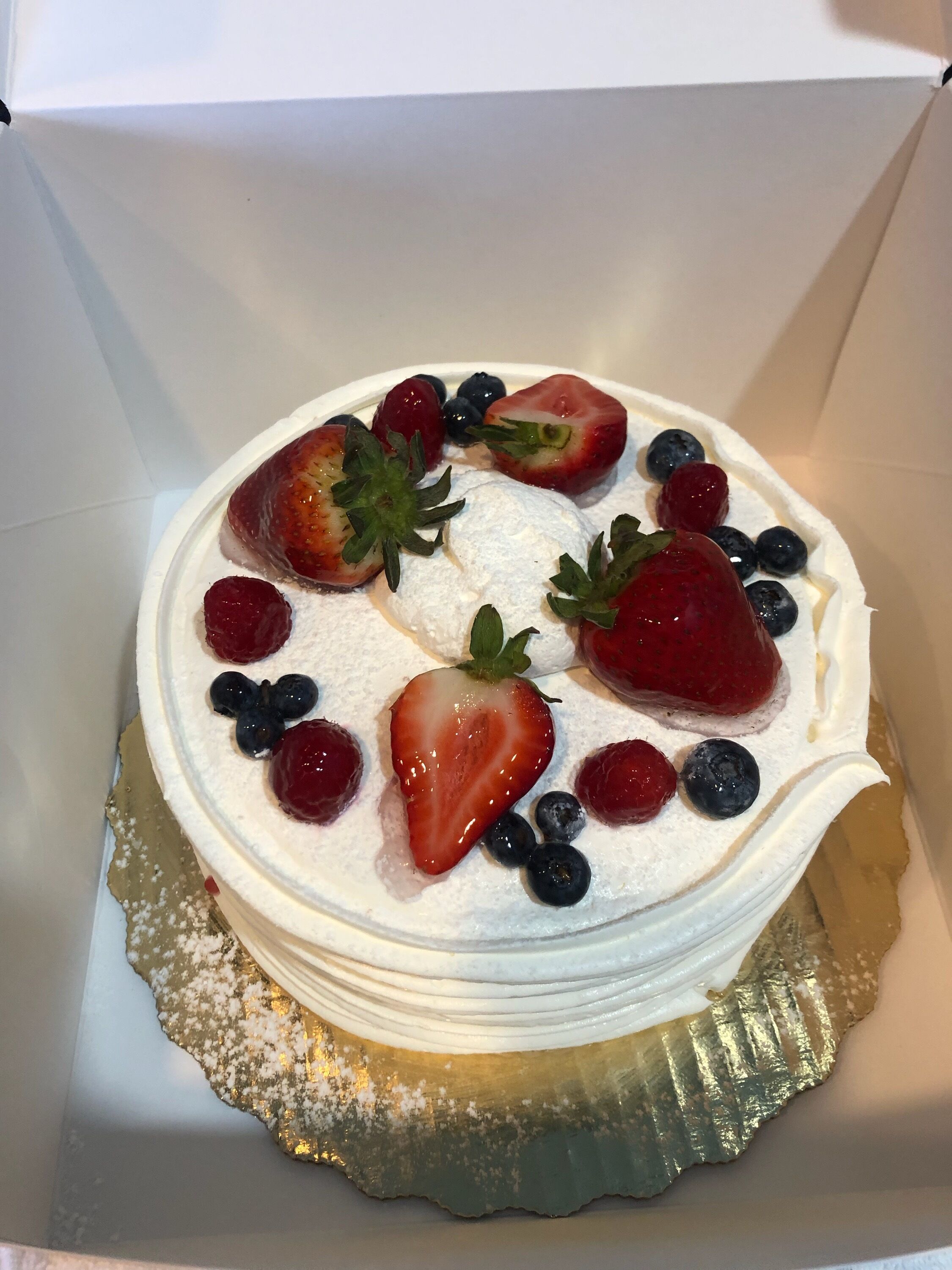 A round cake with white frosting and topped with strawberries and blueberries.