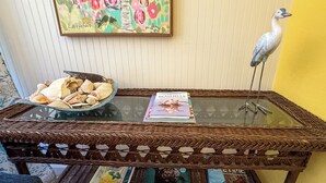 Un tavolino con piano in vetro e base intrecciata, una ciotola con conchiglie e due libri intitolati 'Underwater Dogs' e 'Seashells'.