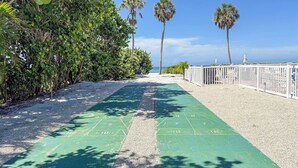 Un campo da shuffleboard verde con una recinzione bianca e palme sullo sfondo.