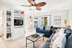 A living room with a TV, white cabinets, a blue sofa, a ceiling fan, and a view of the outdoors. - Silver Sands: Open Tonite - Friday! (Longboat Key)