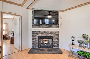 A modern living room with a stone fireplace, a flat-screen TV mounted above it, and a small table with potted plants. - Updated Home Near Neuse River Fishing & Boating (Arapahoe)