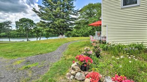 A house with a gravel path leading to a deck, surrounded by lush greenery and a lake. - Ocean Inlet Cottage w/ Deck & Grill! (West, Bath)