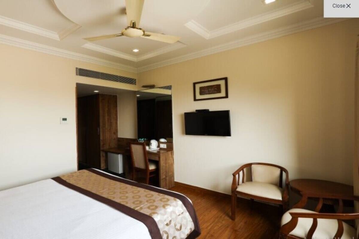 A hotel room with a bed, a desk, a chair, a television, and a ceiling fan.