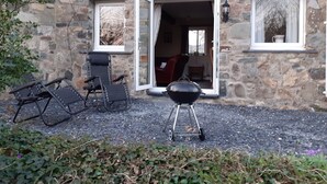 A stone building with an open door, a barbecue grill, and two folding chairs outside. - Inviting 3-bed Cottage Close to Pwllheli (Pwllheli)