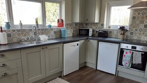 A kitchen with a dishwasher, microwave, oven, and a window with a view of trees. - Inviting 3-bed Cottage Close to Pwllheli (Pwllheli)