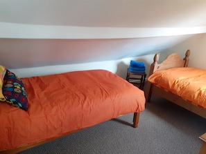 A small, compact room with two single beds, a small wooden chair, and a colorful pillow. - Inviting 3-bed Cottage Close to Pwllheli (Pwllheli)